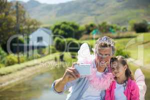 Smiling father and daughter in fairy costume taking selfie on mobile phone