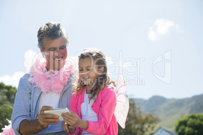 Smiling father and daughter in fairy costume looking photos on mobile phone