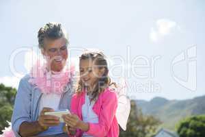 Smiling father and daughter in fairy costume looking photos on mobile phone