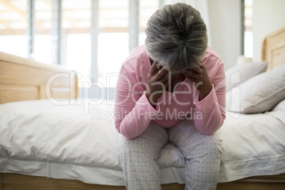 Tense senior woman sitting on bed in bedroom