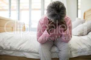 Tense senior woman sitting on bed in bedroom