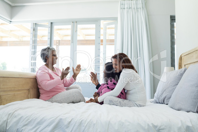 Family playing clapping games on bed in bedroom