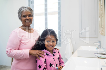 Smiling granddaughter and grandmother standing in bathroom