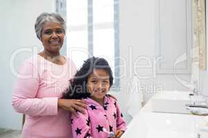 Smiling granddaughter and grandmother standing in bathroom