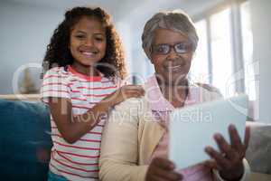 Smiling granddaughter and grandmother holding digital tablet in living room