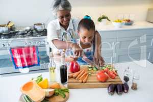 Grandmother assisting granddaughter to chop vegetables in kitchen