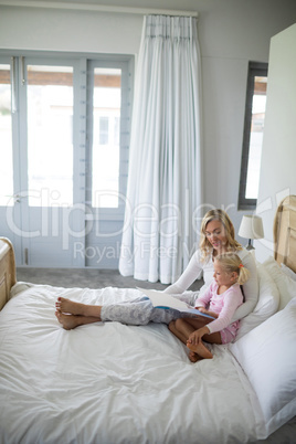 Mother and daughter reading story book in the bedroom