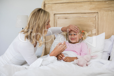 Mother checking sick daughter temperature with digital thermometer in the bedroom