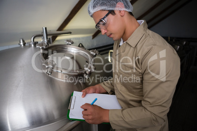 Worker writing on clipboard by storage tank