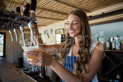 Happy barmaid pouring beer from tap in glass