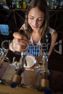 Beautiful barmaid pouring beer from tap in glass