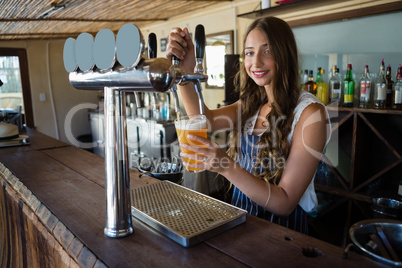 Portrait of young barmaid pouring beer from tap in glass