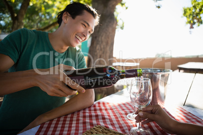 Smiling man pouring wine in glass held by friend