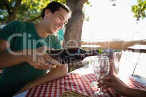 Smiling man pouring wine in glass held by friend