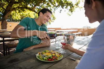 Smiling man pouring wine in glass held by female friend