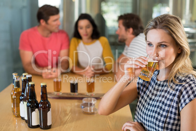 Woman having beer while friends standing in background