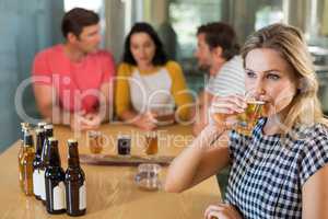 Woman having beer while friends standing in background