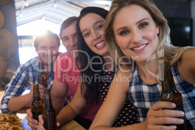 Portrait of smiling friends holding beer bottles at bar counter