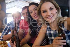 Portrait of smiling friends holding beer bottles at bar counter