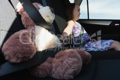 Girl sitting with teddy bear in car back seat