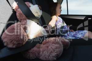 Girl sitting with teddy bear in car back seat