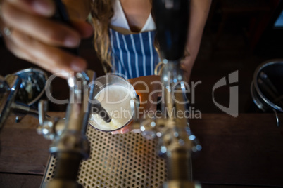 Midsection of barmaid pouring beer from tap in glass