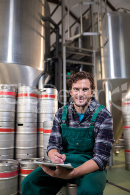 Portrait of smiling worker with clipboard sitting at warehouse