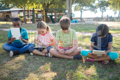 Children using tablet computer while sitting on grassy field