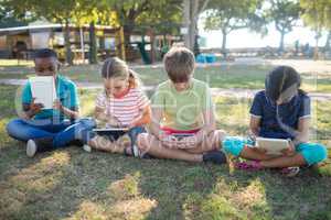 Children using tablet computer while sitting on grassy field