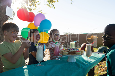 Happy children talking while having food and drinks against sky at table