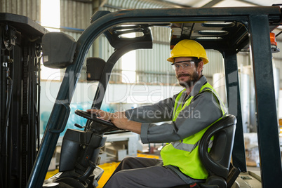 Smiling worker driving a forklift car in factory