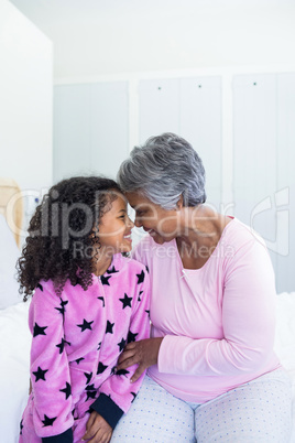 Smiling granddaughter and grandmother sitting face to face on bed