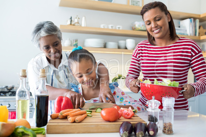 Grandmother assisting granddaughter to chop vegetables in kitchen