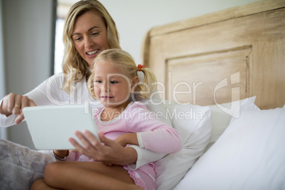 Mother and daughter using digital tablet in the bedroom