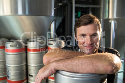 Portrait of smiling worker leaning on kegs at warehouse