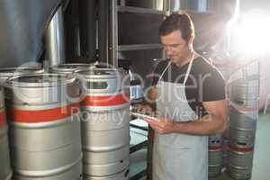 Worker using digital tablet on notepad while standing by kegs