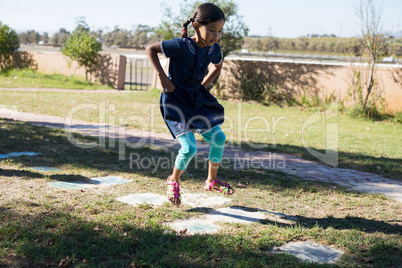 Girl with hands on hip jumping on grassy field