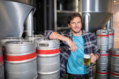 smiling male worker holding beer glass while standing at factory