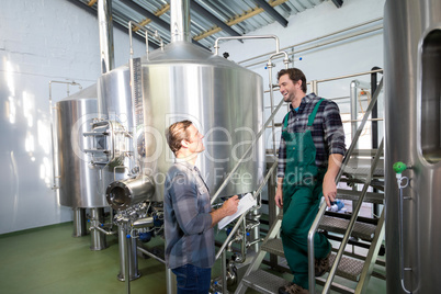 Coworkers discussing while standing by storage tanks at brewery