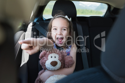 Excited girl holding teddy bear while gesturing in car