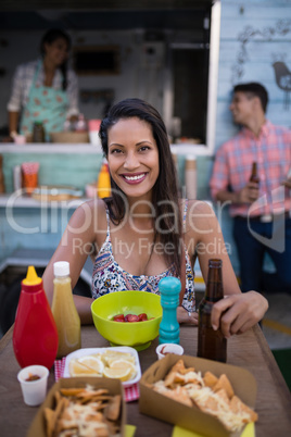 Portrait of beautiful woman holding beer bottle while having snacks