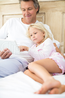 Smiling father and daughter using digital tablet on bed