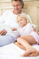 Smiling father and daughter using digital tablet on bed