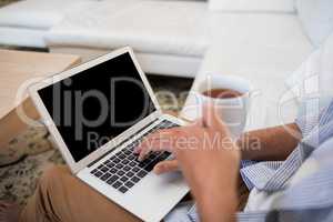 Man using laptop while having coffee in living room