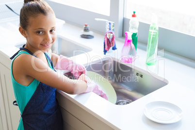 Smiling girl washing plate in kitchen sink