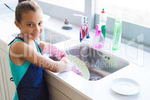 Smiling girl washing plate in kitchen sink