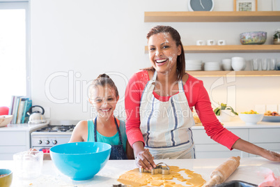 Smiling mother and daughter preparing cookies in kitchen worktop