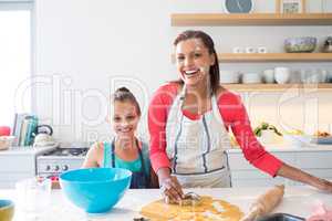 Smiling mother and daughter preparing cookies in kitchen worktop