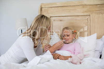 Mother checking sick daughter temperature with digital thermometer in the bedroom