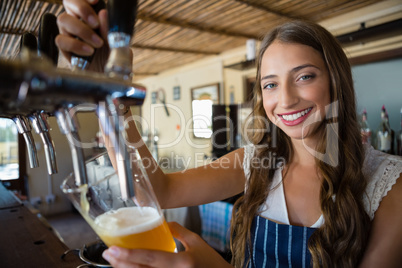 Portrait of smiling barmaid pouring beer from tap in glass